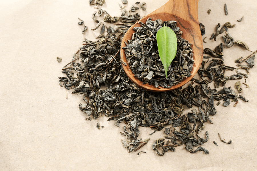 green tea leaves furled and wooden spoon with one fresh tea leaf
