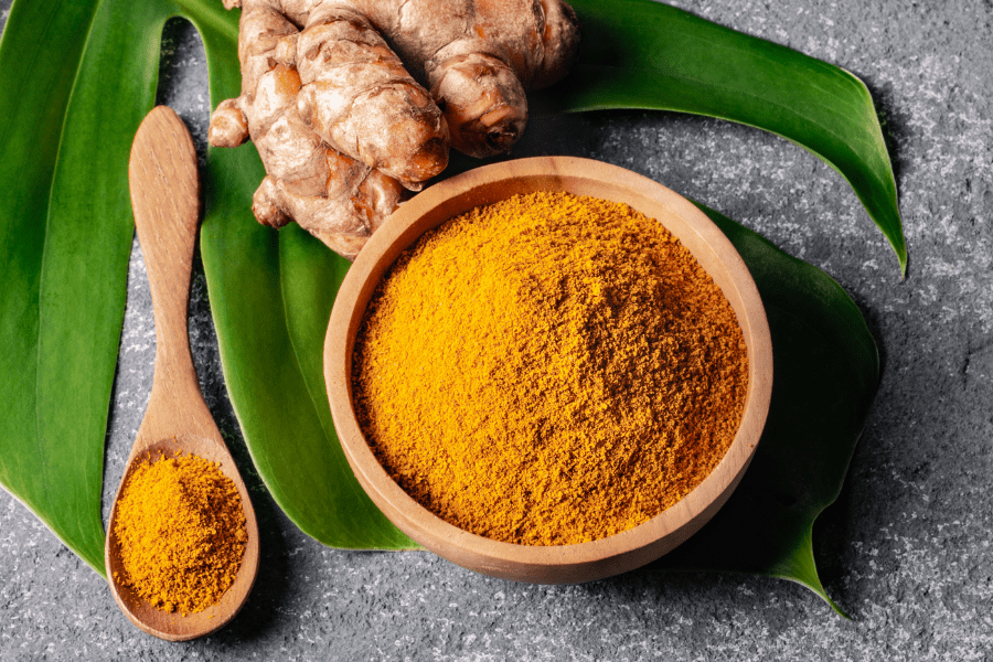 anti-inflammatory herbs turmeric roots and ground turmeric spice in wood bowl