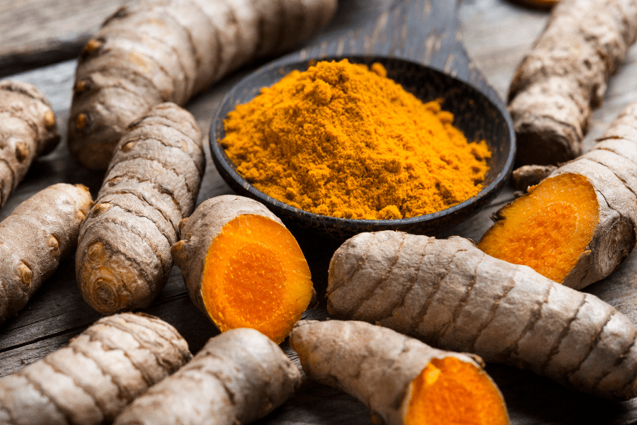 anti-inflammatory turmeric gut healing spice: whole turmeric roots, and powdered turmeric in wood spoon